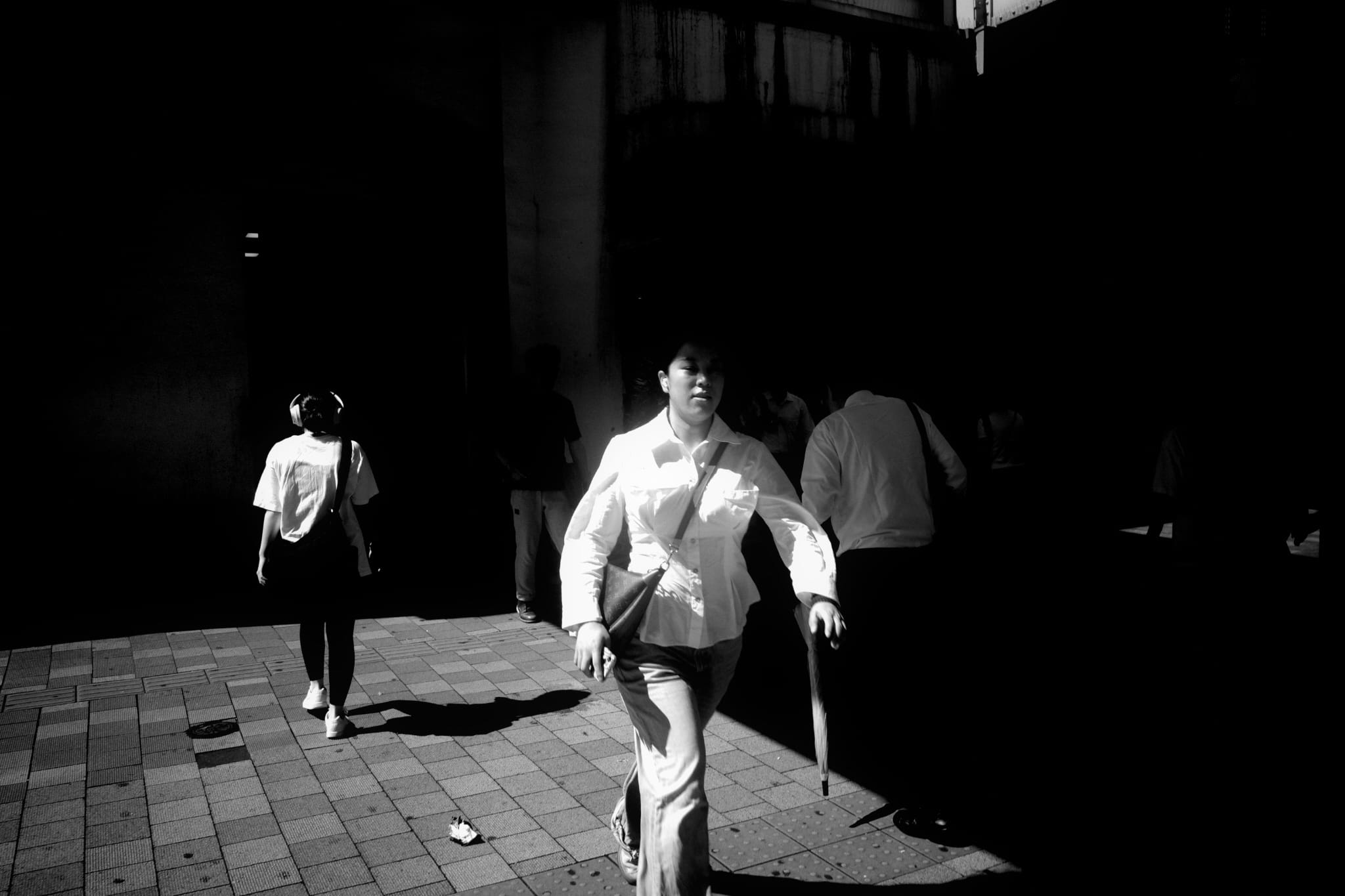 Pedestrians crossing a dark plaza in hard sunlight